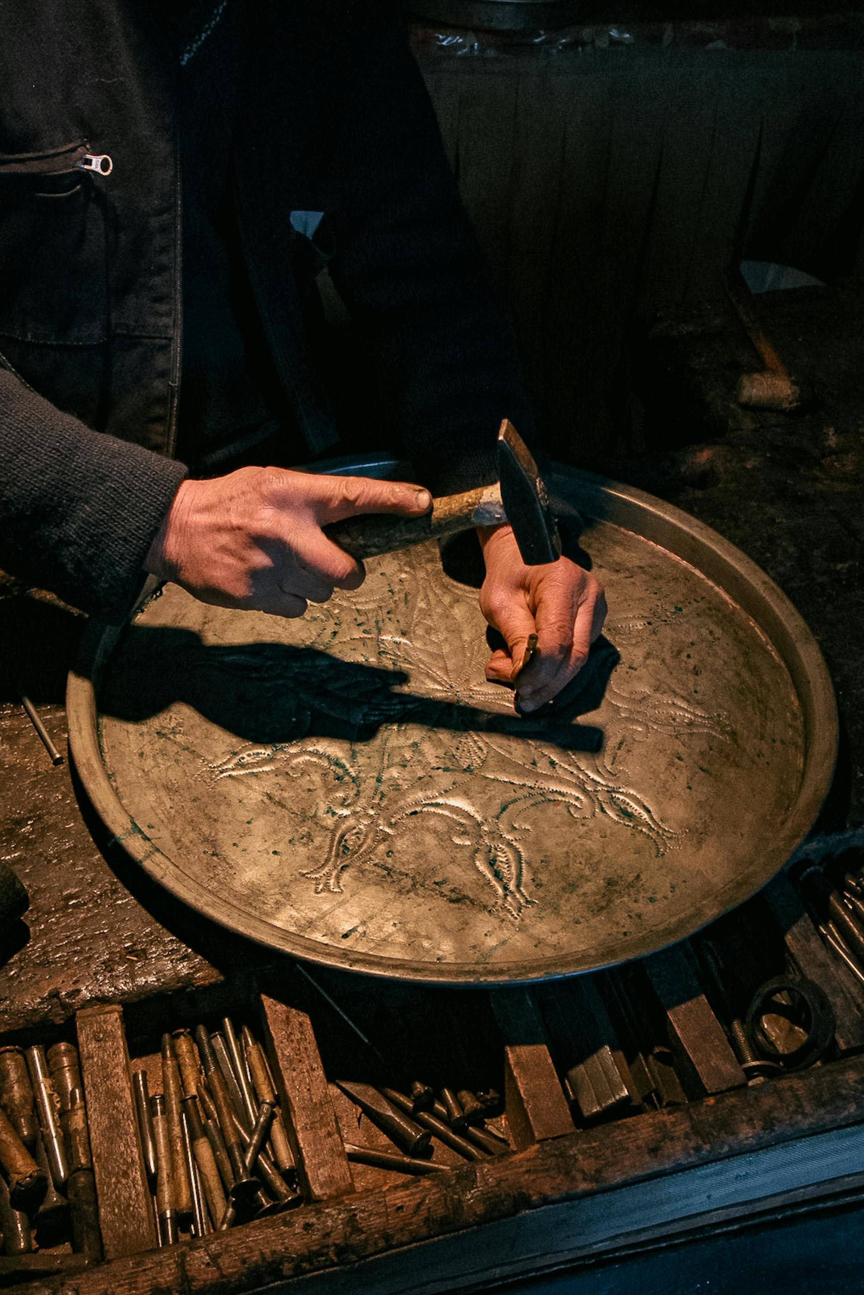 Close-up of artisan crafting a decorative plate with hammer in a workshop in Denizli, Türkiye.